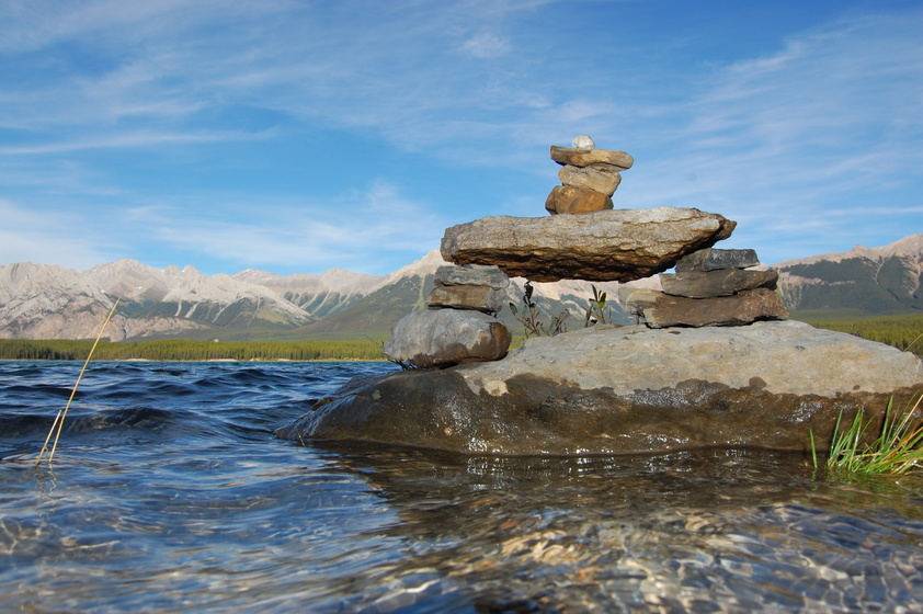 A pile of rocks juts out of the calm water of a mountain lake.