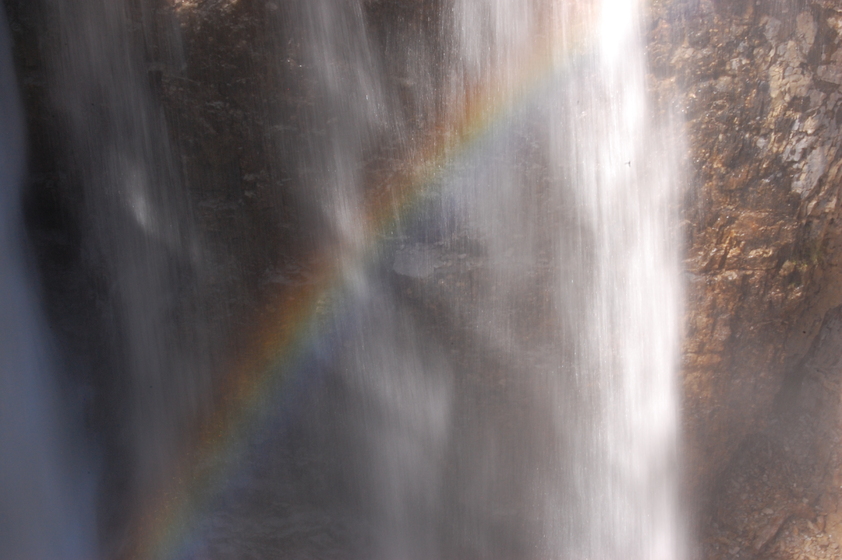 A waterfall with sunlight shining through, creating a rainbow effect in the mist.